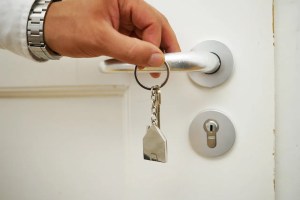 Χέρι ξεκλειδώνει πόρτα με κλειδί σε σχήμα σπιτιού