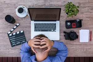 Άντρας με τα χέρια στο κεφάλι μπροστά σε λάπτοπ