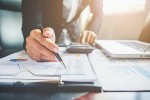 Χέρι με στυλό δίπλα σε αριθμομηχανή και γραφήματα