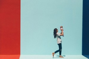 Γυναίκα σηκώνει ψηλά το μωρό της μπροστά σε χρωματιστό τοίχο