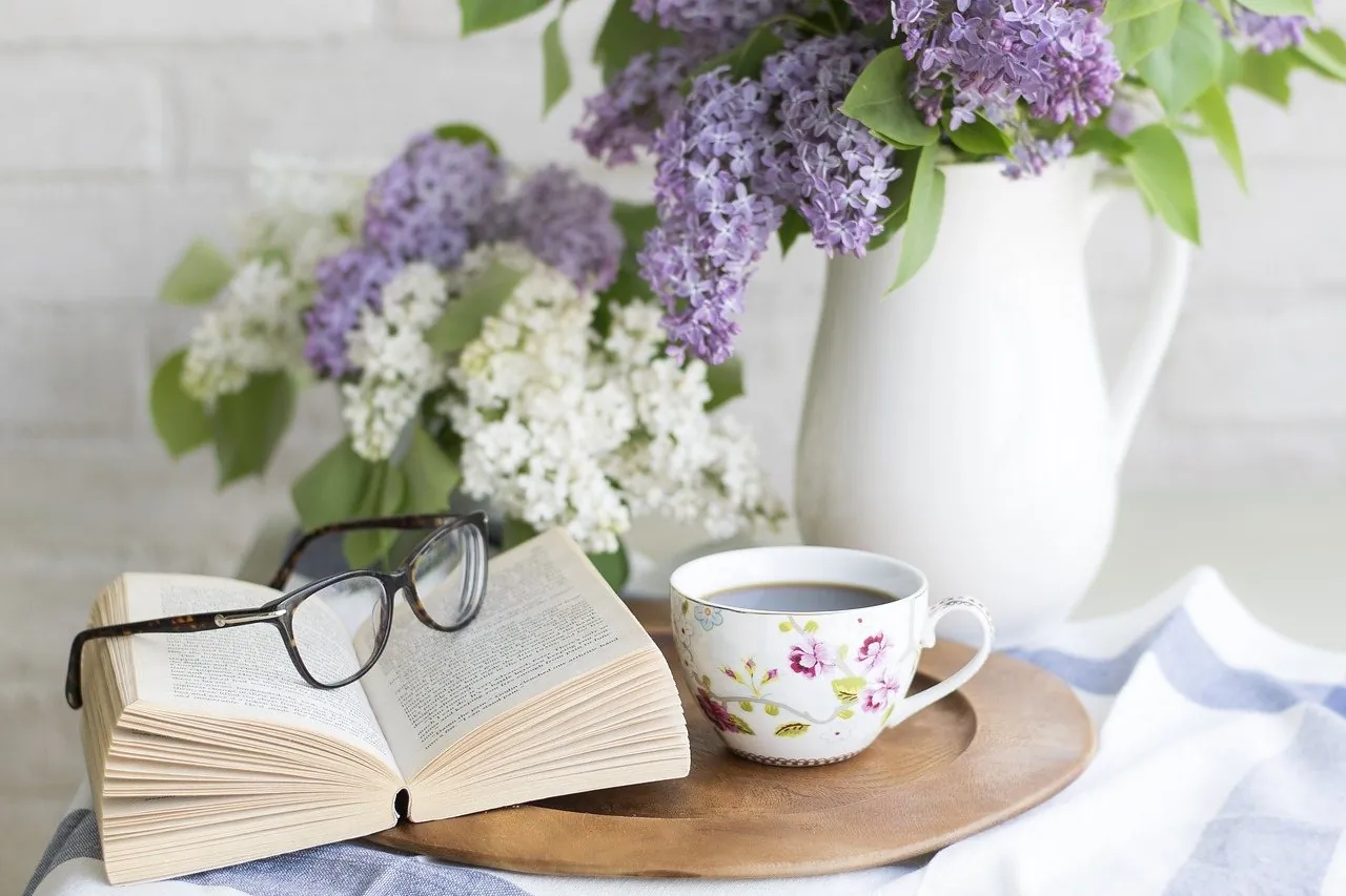 Открытая книга с очками рядом с чашкой кофе и сиренью